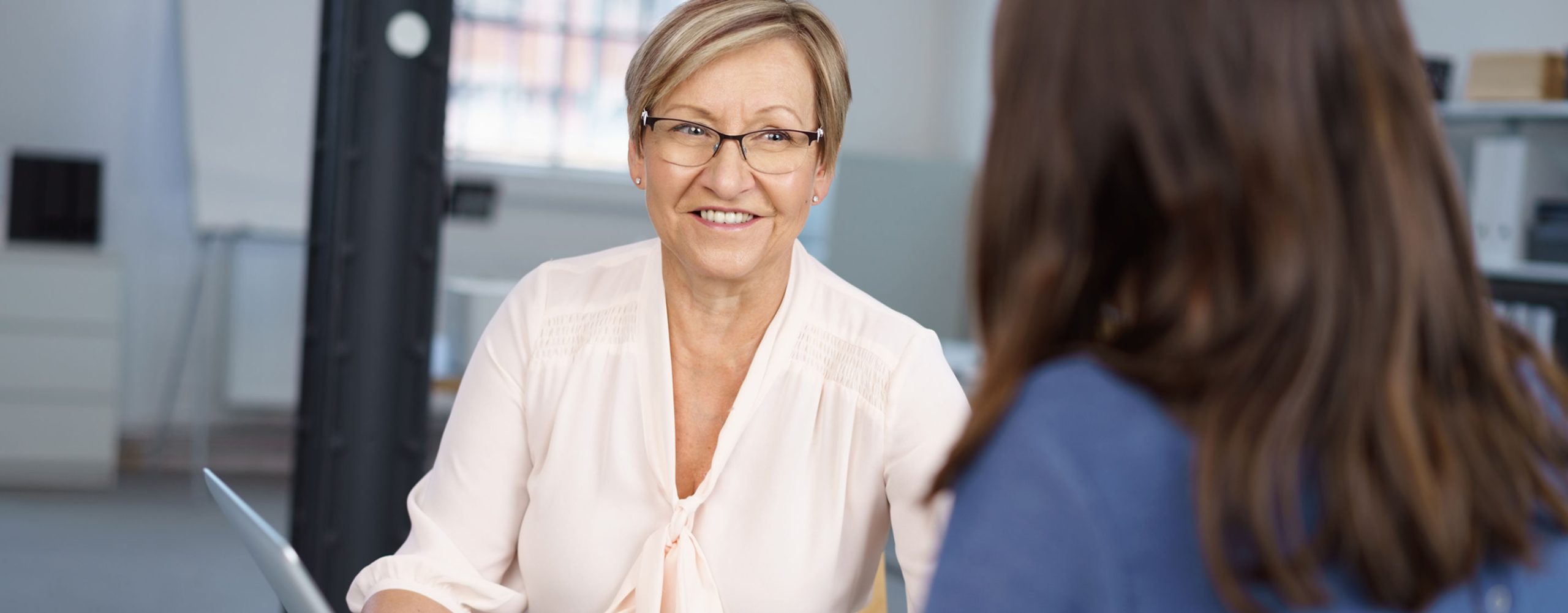 Zwei Frauen sitzen sich in einem Büro gegenüber und führen ein Gespräch.