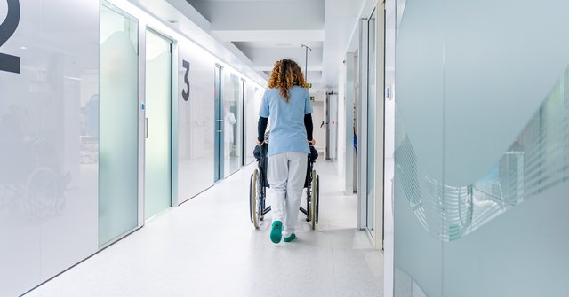 Krankenhausflur mit Pflegerin, die einen Rollstuhl schiebt