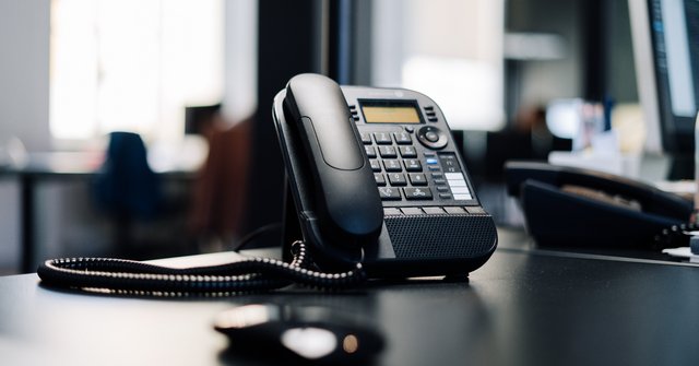 Ein schwarzes Telefon auf einem Schreibtisch.